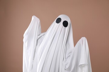Creepy ghost. Person covered with white sheet on dark beige background