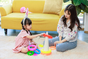 Happy asian mother and cute little daughter wearing bunny ears headbands builds rainbow tower while playing on floor of children's room, Mom and girl have fun. Concept of parenting child development.