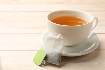 Tea bag and cup of hot beverage on light wooden table, closeup. Space for text