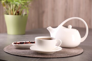 Aromatic tea in cup, saucer, teapot and dry flower petals on grey table