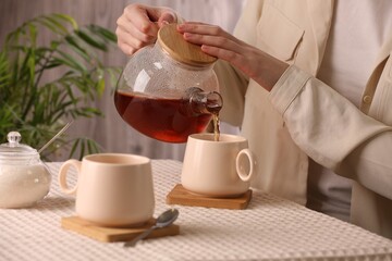 Woman pouring aromatic tea into cup at table, closeup