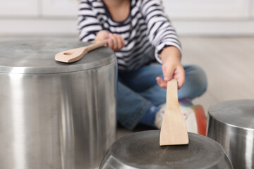 Little girl pretending to play drums on pots indoors, closeup