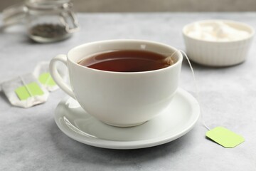 Tea bags and cup of hot beverage on light table, closeup