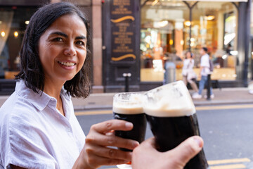 Latin woman enjoying her stay on the streets of Dublin drinking a Guinness and toasting with her...