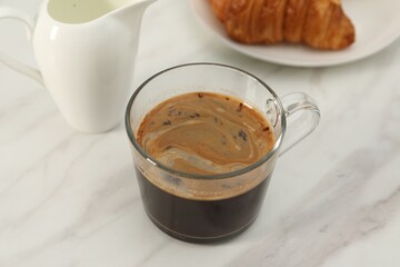Aromatic coffee in glass cup and pitcher on white marble table, closeup