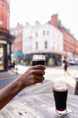 Close-up of hand raising a Guinness against the background of a beautiful Dublin street on a bright...