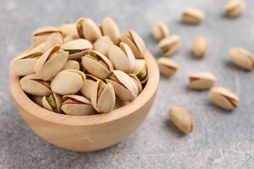 Delicious pistachios in bowl on grey textured table