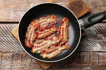 Delicious bacon slices in frying pan on wooden table, top view