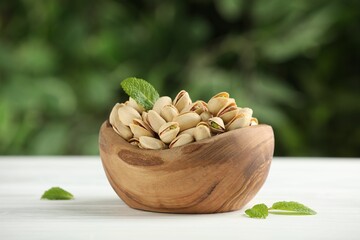 Tasty pistachios in bowl on white table against blurred background