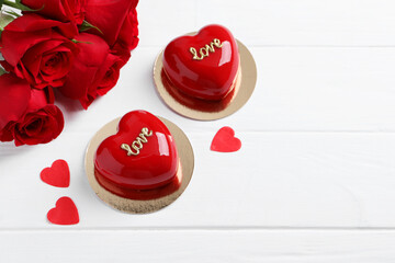 St. Valentine's Day. Delicious heart shaped cakes and beautiful roses on white wooden table, above view. Space for text