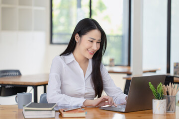 Happy asian young businesswoman using laptop at workplace.