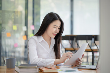 Happy asian young businesswoman holding documents folders in office working space, Asian female employee using laptop talking on the phone at workplace. - obrazy, fototapety, plakaty