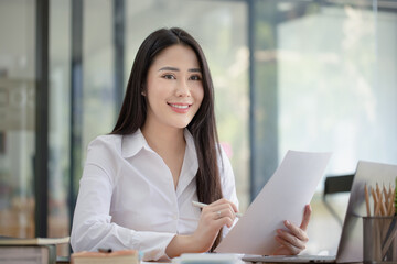 Happy asian young businesswoman holding documents folders in office working space, Asian female employee using laptop talking on the phone at workplace.
