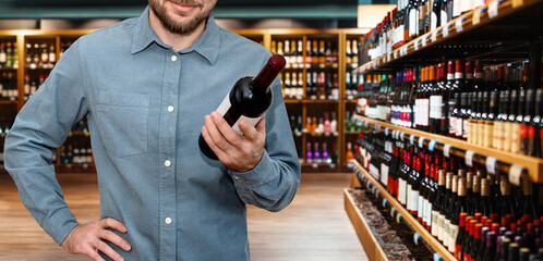 man customer chooses the wine in liquor store. Male person holding red wine bottle in hand on...