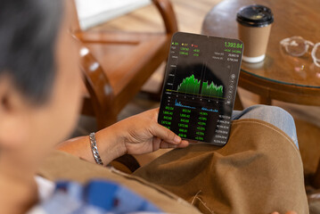 Senior, elderly, retired, woman looking graph stock exchange market on digital tablet at her coffee shop. Startup and Small business, Business owner. Investment concept, Wireless and 5G technology.
