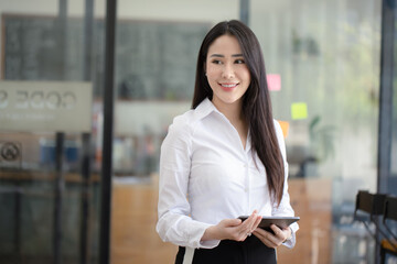 Happy asian young businesswoman using digital tablet standing in office office working space.