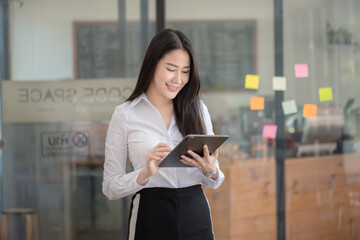 Happy asian young businesswoman using digital tablet standing in office office working space.