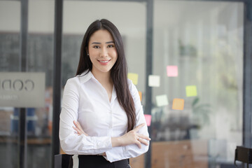 Happy asian young businesswoman arms crossed standing in office working space.