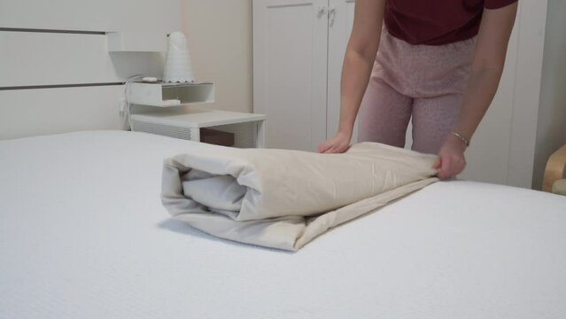 woman folding fitted sheet on bed in bedroom