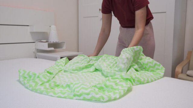 woman folding fitted sheet on bed in bedroom