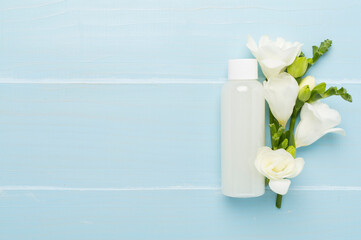 Cosmetic bottle with freesia flowers on wooden background, top view