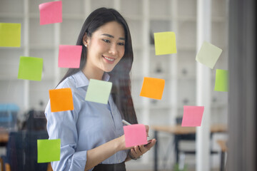 Startup successful asian businesswoman working with sticky note on glass wall and meeting to share...