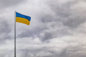 A large national flag of Ukraine fluttering in the wind on a flagpole, against the backdrop of a cloudy sky with dark clouds