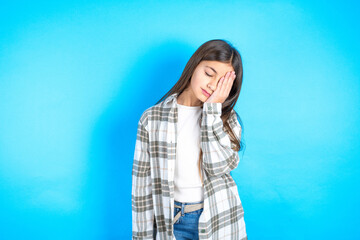 Tired overworked Young beautiful teen girl wearing check shirt has sleepy expression, gloomy look, covers face with hand, has eyes shut, gasps from tiredness, fatigue after party