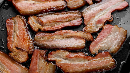 Fresh frying bacon top view. Delicious crispy bacon strips cooking on a flat top grill
