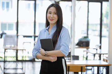 Happy asian young businesswoman holding a digital tablet standing in office office working space.