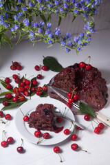 Chocolate cake with sweet cherry, cup of tea and bouquet of blue flowers on white background..