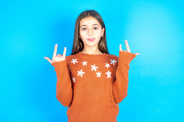 Young beautiful teen girl wearing orange knitted sweater makes rock n roll sign looks self...