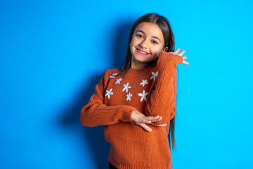 Overjoyed successful Young beautiful teen girl wearing orange knitted sweater raises palm and...