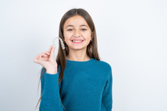 Young beautiful teen girl wearing blue T-shirt holding an invisible braces aligner, recommending this new treatment. Dental healthcare concept.