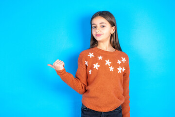 Young beautiful teen girl wearing orange knitted sweater points away and gives advice demonstrates...