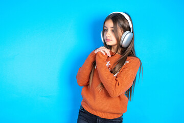Young beautiful teen girl wearing orange knitted sweater wears stereo headphones listening to music...