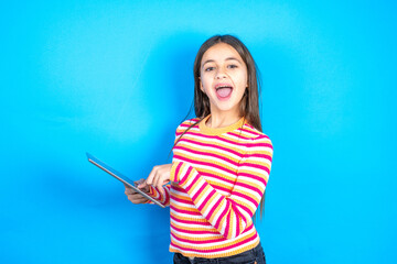 Photo of happy cheerful smart Young kid girl wearing striped t-shirt hold tablet browsing internet