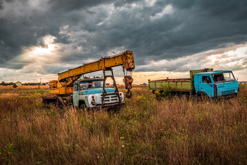 Abandoned construction crane truck and old truck under stormy clouds