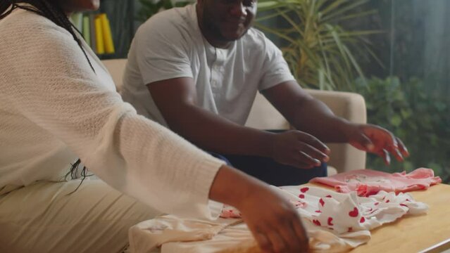 Medium shot of young black mother-to-be and her husband preparing clothes for baby before going to birthing centerMedium shot of young black mother-to-be and her husband preparing clothes for baby bef