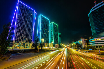Fototapeta na wymiar Neon light on modern skyscrapers and avenue traffic in Kyiv