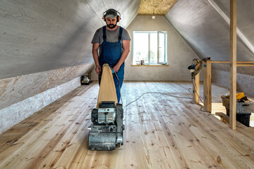 Professional worker carpenter grinding sanding a wooden floor by using floor sander. Industrial theme