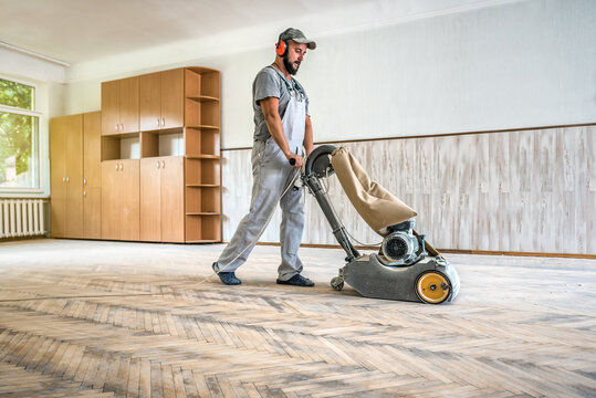 Professional worker carpenter grinding sanding cleaning a wooden floor by using floor sander. Industrial theme