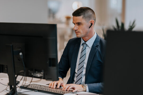 Confident young businessman typing while using computer at desk in office