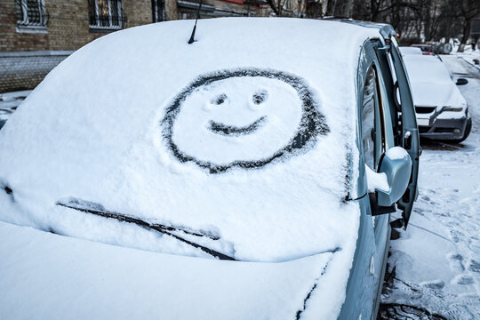 Smiling face (symbol) painted on snow above windshield wiper of car. Winter, transport concept.