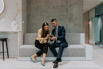 Full length of male and female delegates sitting on sofa sharing smart phone during seminar