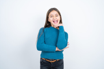 Optimistic beautiful kid girl wearing blue sweater keeps hands partly crossed and hand under chin, looks at camera with pleasure.