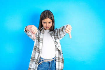 Beautiful kid girl wearing plaid shirt  being upset showing thumb down with two hands. Dislike concept.