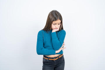 Very bored beautiful kid girl wearing blue sweater holding hand on cheek while support it with...