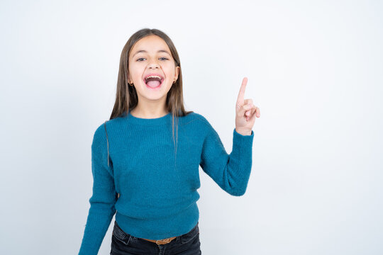 beautiful kid girl wearing blue sweater holding finger up having idea and posing