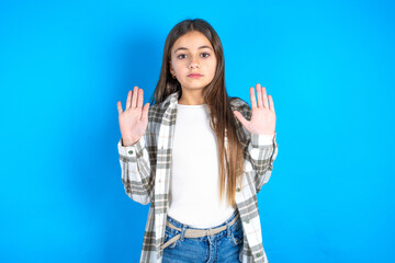 Serious Beautiful kid girl wearing plaid shirt pulls palms towards camera, makes stop gesture, asks...